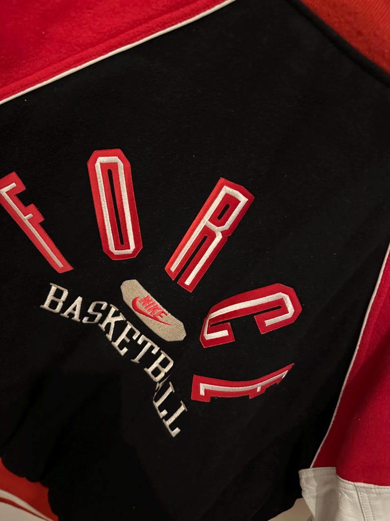 May include: Black and red basketball jacket with the word "FORCE" in red and white lettering. The word "BASKETBALL" is embroidered in white. A Nike logo is visible.