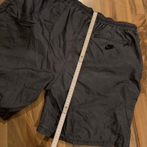 May include: Dark gray nylon athletic shorts with a black Nike logo on the back right pocket. The shorts have a drawstring waist and a zippered pocket on the right side.