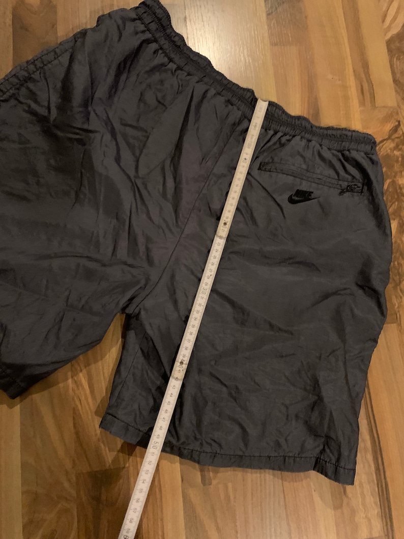 May include: Dark gray nylon athletic shorts with a black Nike logo on the back right pocket. The shorts have a drawstring waist and a zippered pocket on the right side.