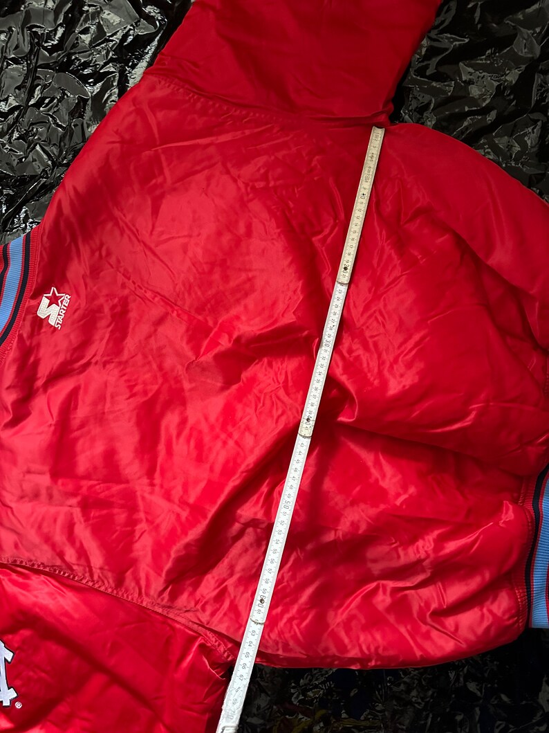 May include: Red satin bomber jacket with a blue and white striped collar and cuffs. The jacket has a white "Starter" logo on the left chest.