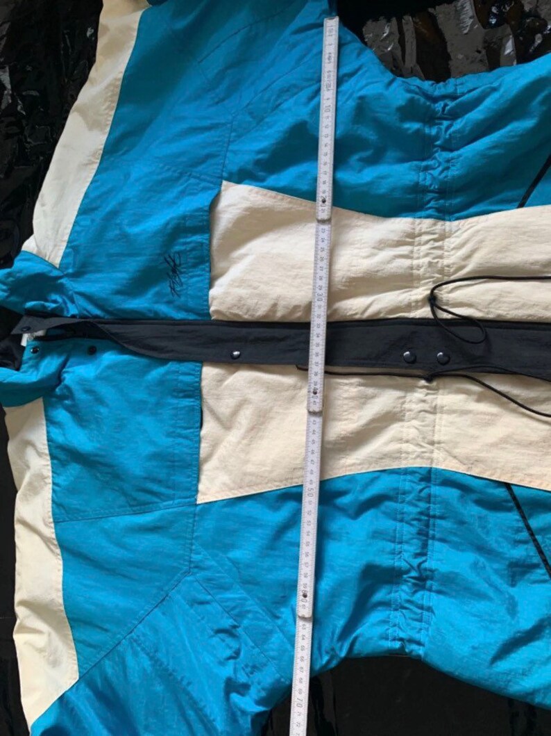 May include: A blue, white, and black jacket with a zipper closure and a drawstring at the waist.