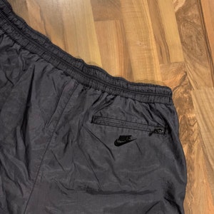 May include: Black nylon athletic shorts with a zippered pocket on the back right side. The pocket has a black Nike logo.