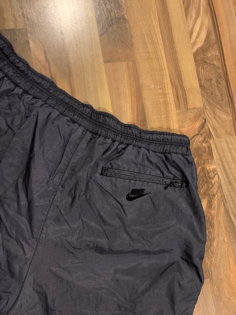 May include: Black nylon athletic shorts with a zippered pocket on the back right side. The pocket has a black Nike logo.