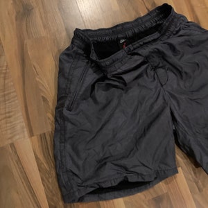 May include: Black athletic shorts with a drawstring waist and a zippered pocket on the side. The shorts have a Nike logo on the waistband.