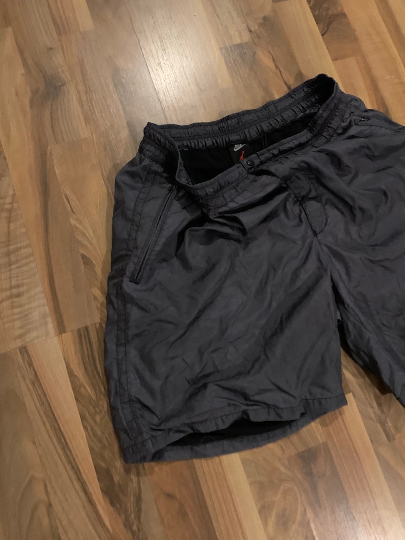 May include: Black athletic shorts with a drawstring waist and a zippered pocket on the side. The shorts have a Nike logo on the waistband.