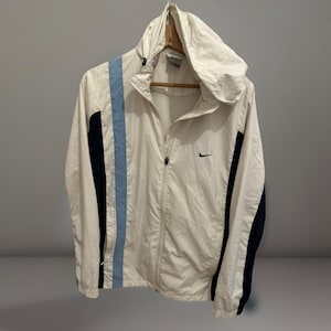 Puede incluir: Chaqueta con capucha Nike blanca con cremallera completa. La chaqueta presenta una franja azul claro en el lado izquierdo y paneles azul marino en las mangas. Peque&ntilde;o logotipo negro de Nike en el pecho.