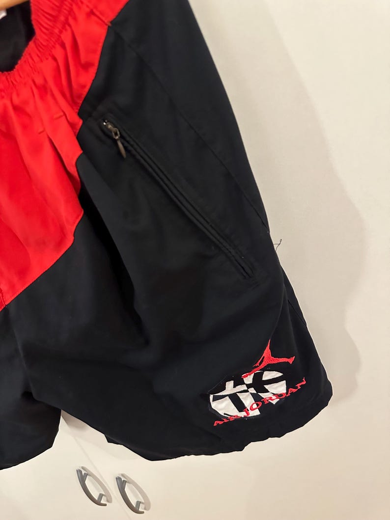 May include: Black and red athletic shorts with a zippered pocket and a red embroidered logo that says "Air Jordan" on the right leg.