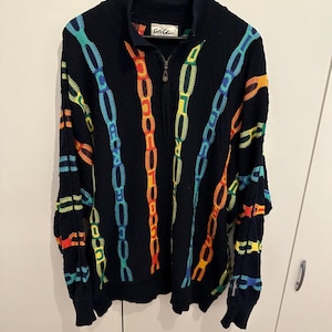Könnte beinhalten: Marineblauer Pullover mit Reißverschluss und farbenfrohem Kettenmuster in Orange, Gelb, Blau und Grün. Der Pullover hat einen hohen Kragen und die Marke "Cote Ciel" ist sichtbar.