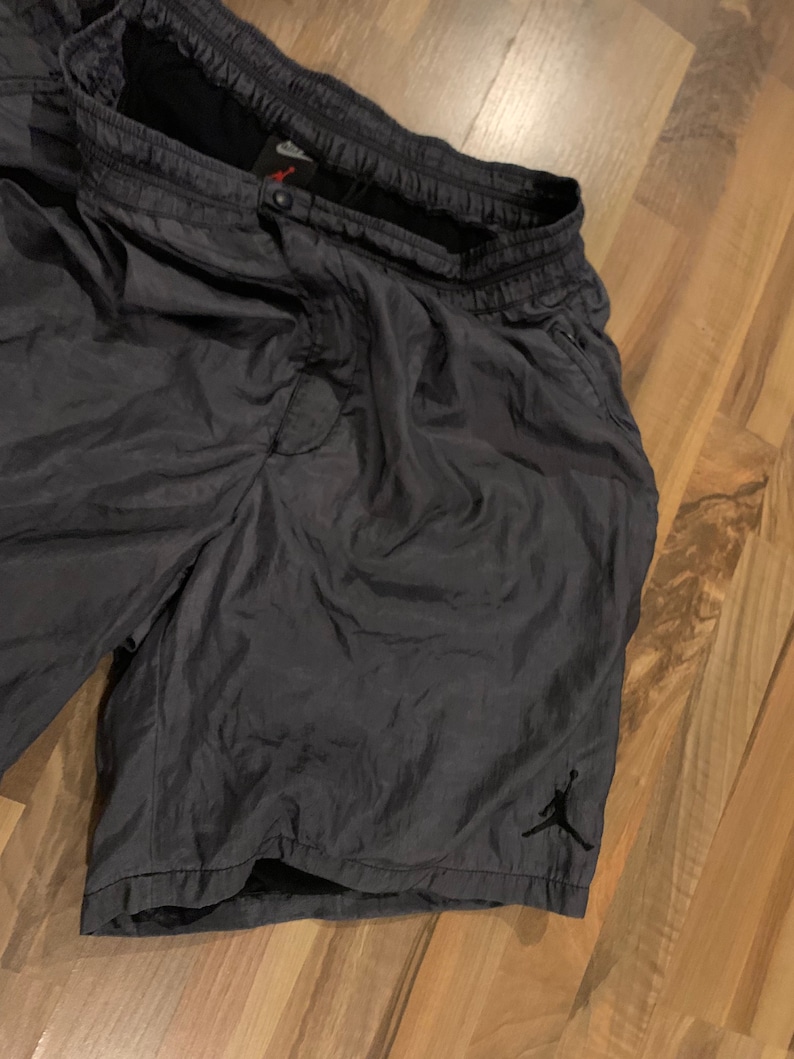 May include: Dark gray athletic shorts with a black Jumpman logo on the right leg. The shorts have a drawstring waistband and side pockets.