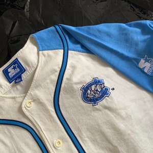 May include: White baseball jersey with blue and black trim. The jersey has a blue and white Starter logo on the right sleeve and a Carolina Tar Heels logo on the front.
