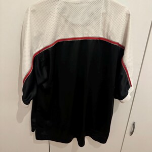 Peut inclure: Veste de sport noire et blanche avec une bande rouge au dos. La veste a un haut du dos et des manches en mesh blanc, une partie inf&eacute;rieure noire et un col blanc. Les manches sont courtes, s'arr&ecirc;tant juste en dessous du coude.