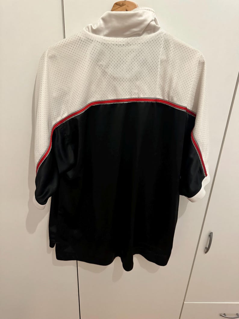 Peut inclure: Veste de sport noire et blanche avec une bande rouge au dos. La veste a un haut du dos et des manches en mesh blanc, une partie inf&eacute;rieure noire et un col blanc. Les manches sont courtes, s'arr&ecirc;tant juste en dessous du coude.