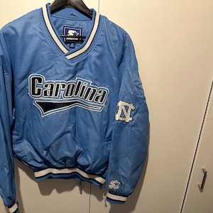 K&ouml;nnte beinhalten: Eine hellblaue Vintage-Starterjacke mit einem Carolina-Logo und einem UNC Tar Heels-Logo am &Auml;rmel.