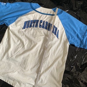 May include: White and light blue baseball jersey with the text "NORTH CAROLINA" in navy blue lettering on the back.