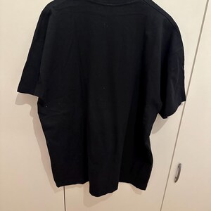 May include: A plain black t-shirt hanging on a black hanger. The short-sleeved shirt is made of a soft material and is displayed against a white background. The shirt is a basic, versatile garment.