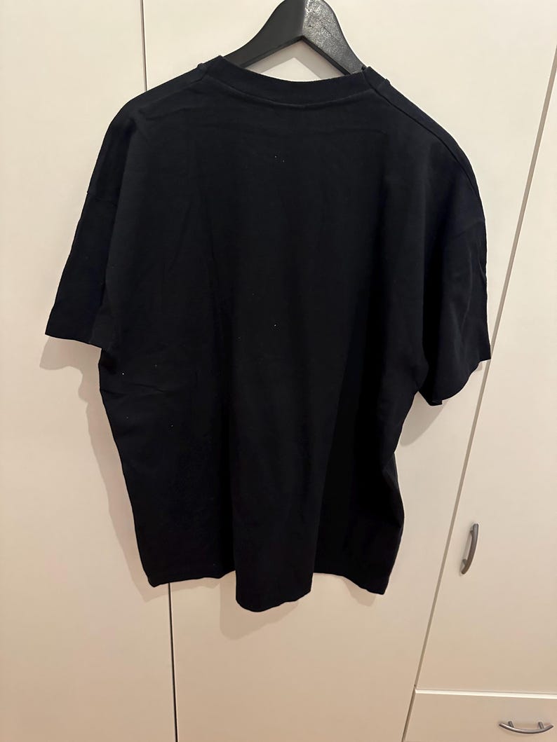 May include: A plain black t-shirt hanging on a black hanger. The short-sleeved shirt is made of a soft material and is displayed against a white background. The shirt is a basic, versatile garment.