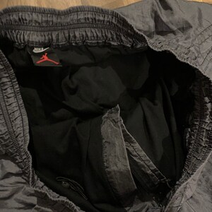 May include: Gray athletic shorts with a black waistband and a Nike logo with the Jumpman logo. The shorts have a drawstring and a zippered pocket.