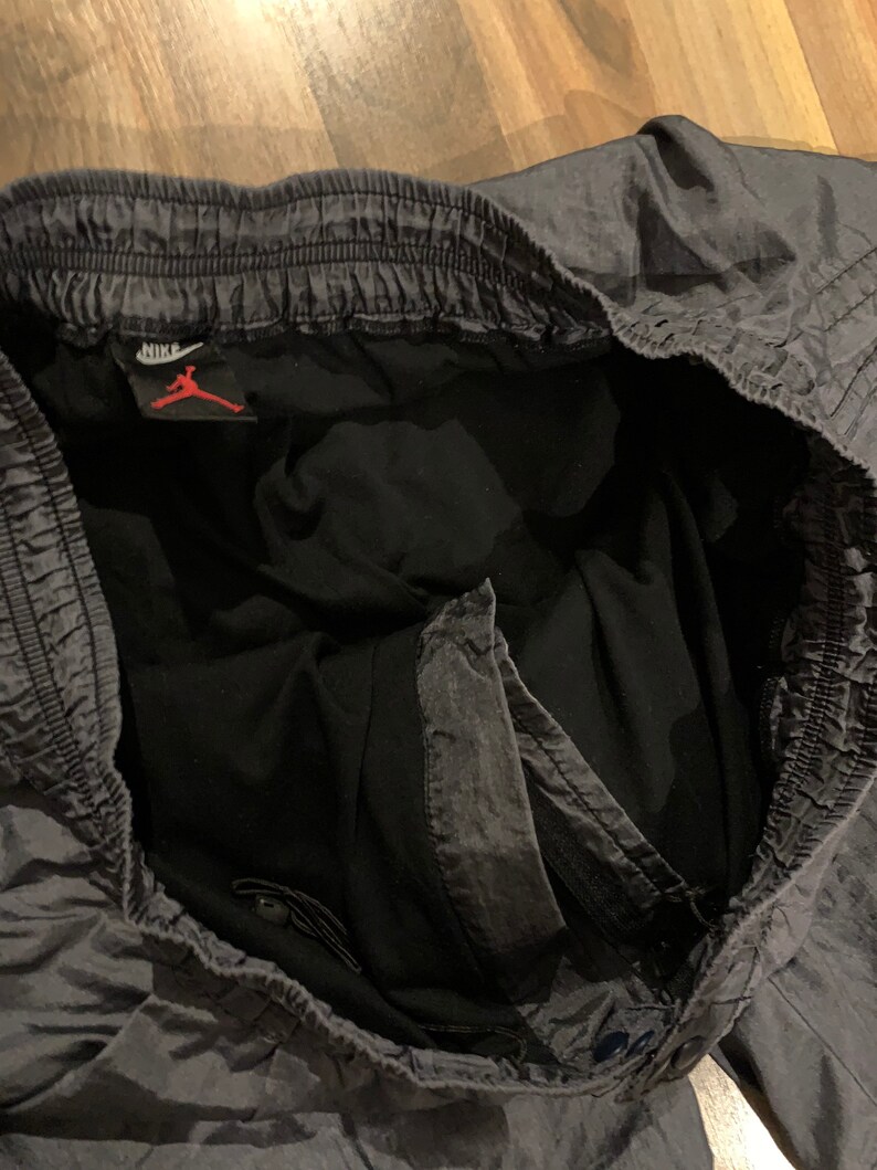 May include: Gray athletic shorts with a black waistband and a Nike logo with the Jumpman logo. The shorts have a drawstring and a zippered pocket.