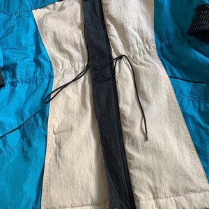 May include: A blue, white, and black jacket with a drawstring waist and a zipper closure. The jacket has a quilted lining.