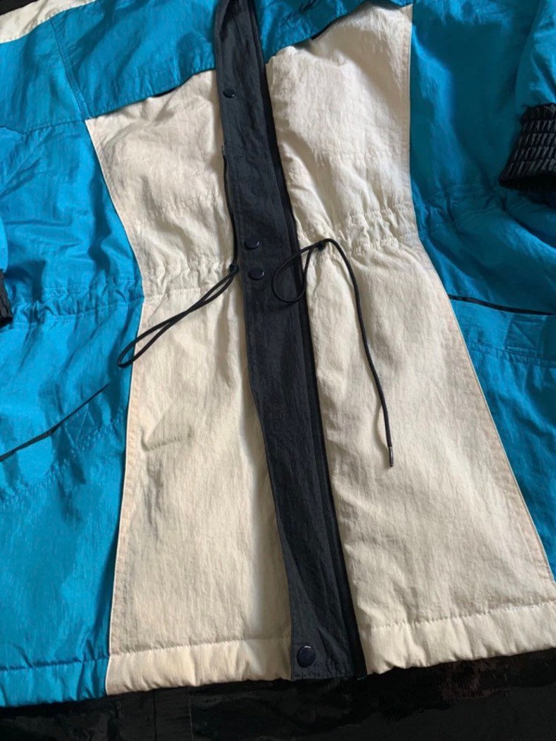 May include: A blue, white, and black jacket with a drawstring waist and a zipper closure. The jacket has a quilted lining.