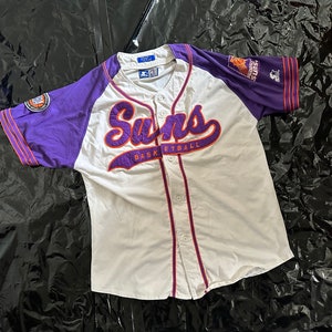Può includere: Maglia da basket dei Suns bianca e viola. La parola "Suns" è ricamata in viola sul petto, con "Basketball" sotto. La maglia ha maniche viola e un'abbottonatura. Articolo sportivo vintage.