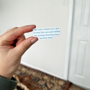 May include: A white sticker with blue text that reads "Not until I looked into a pair of ocean blue eyes and realized that perhaps drowning was a beautiful thing."