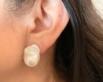 May include: A single white baroque pearl earring with an irregular, organic shape and a lustrous, iridescent surface. The pearl features a smooth, bumpy texture with subtle cream and pink undertones, securely attached to the earlobe.