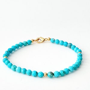 May include: A beaded bracelet featuring small, faceted turquoise-colored stones with a matte finish. The bracelet is accented with three smooth, polished gold-toned metal beads and is secured with a gold-toned lobster claw clasp closure.