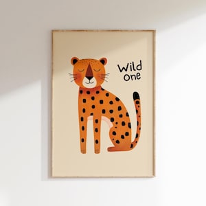 May include: A framed print featuring a cartoon cheetah with orange fur and black spots, sitting on a beige background. The text "Wild one" is written in black. The artwork is in a wooden frame.