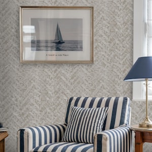 May include: A nautical-themed living room featuring a striped armchair in navy and white, complemented by a matching pillow. A framed sailboat art piece hangs on the textured wall. A navy blue lamp and a small side table complete the scene.