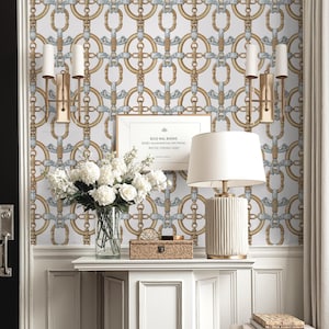 May include: An interior scene with a white console table, lamp, flowers, and framed print. The wall features a repeating pattern of gold and blue chain links. A patterned rug and a small stool with books add to the elegant decor. The room has a classic feel.