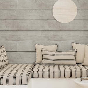 May include: A cozy seating area with a light gray wood-paneled wall and a white circular wall decoration. The built-in bench features striped cushions and pillows in cream and black. A small white side table holds books.