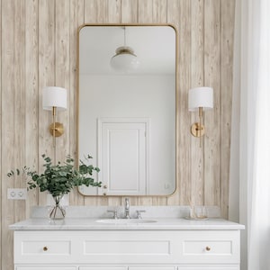 May include: A white bathroom vanity with gold hardware and a marble countertop. A large rectangular mirror with a gold frame hangs above the vanity. The wall behind the mirror is covered in vertical wood paneling. Two gold sconces flank the mirror.