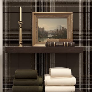May include: A bathroom shelf display featuring stacked green and white towels, a framed landscape painting, and a gold candlestick with a lit candle. The backdrop is a brown plaid wallpaper.