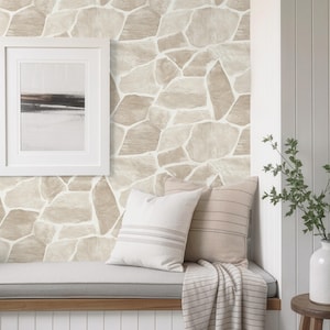 Puede incluir: Escena interior acogedora con una pared con patrón de piedra, una obra de arte enmarcada y un banco empotrado con cojines y una manta a rayas. Un pequeño taburete de madera sostiene un jarrón blanco con vegetación.