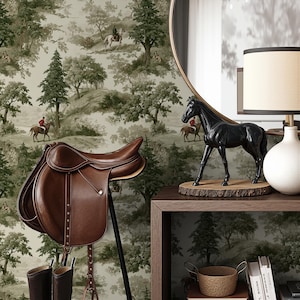 May include: A brown leather English saddle with stirrups and a matching pair of riding boots. A black horse statue sits on a wooden base on a dark wood table. The background features a wallpaper with a forest scene.