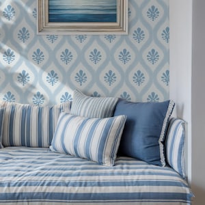 Può includere: Un'accogliente area salotto con cuscini a righe blu e bianche e una base a righe abbinata. I cuscini sono in varie tonalità di blu e bianco. La parete posteriore presenta un motivo floreale azzurro e un dipinto di paesaggio marino incorniciato.