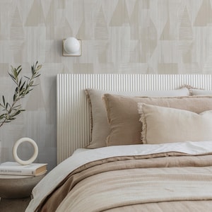 Könnte beinhalten: Ein Schlafzimmer mit einem Bett mit beiger Bettwäsche und Kissen. Das Kopfteil ist weiß mit vertikalen Linien. Die Wand hat ein geometrisches Muster in Beige und Weiß. Eine weiße Lampe und ein kleiner Beistelltisch mit einem Buch und einem dekorativen Ring sind ebenfalls zu sehen.