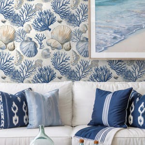 Puede incluir: Sal&oacute;n de tem&aacute;tica costera con un sof&aacute; blanco con cojines azules estampados y una mesa de centro de mimbre. La pared est&aacute; decorada con papel pintado de conchas marinas y corales. Una imagen enmarcada del mar y la playa est&aacute; en la pared.