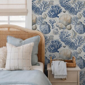 Puede incluir: Decoraci&oacute;n de dormitorio con tem&aacute;tica costera. Cama con cabecero de mimbre, ropa de cama azul claro y cojines estampados. La pared est&aacute; decorada con un dise&ntilde;o de conchas marinas y corales azules y beige. Mesita de noche con cesta y manta a rayas.