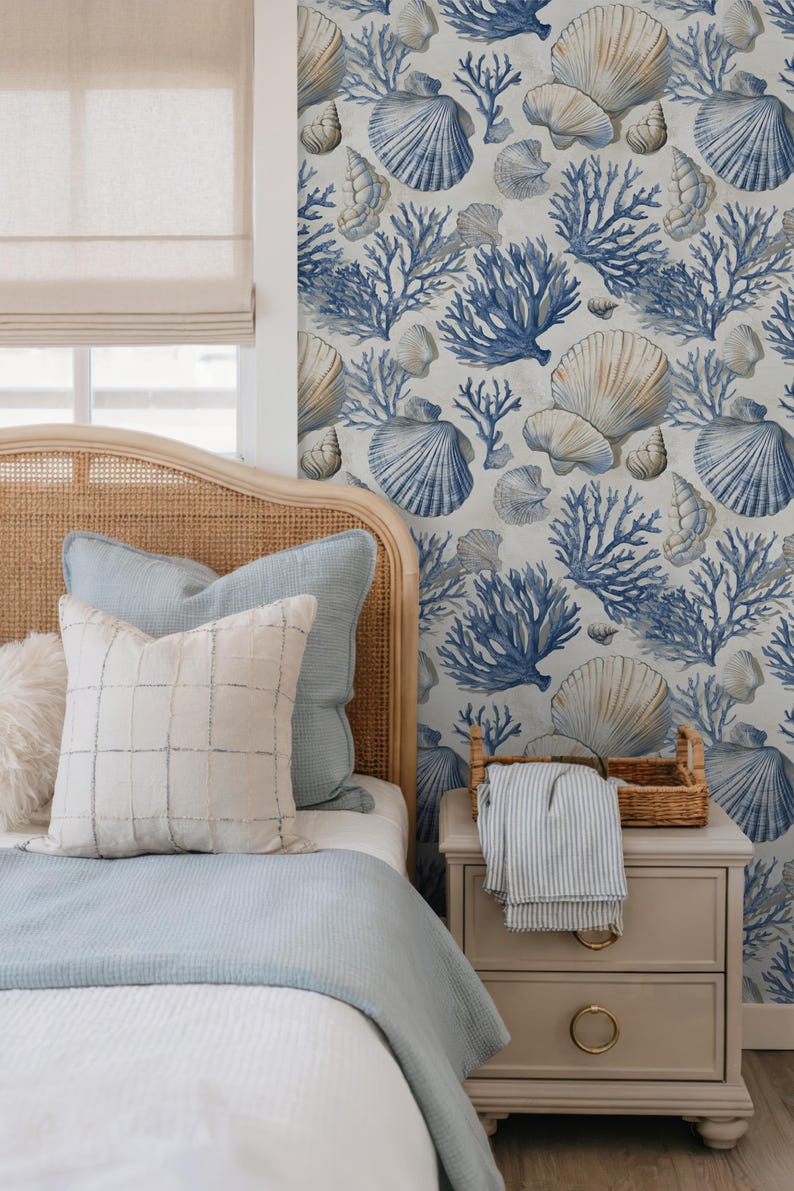 Puede incluir: Decoraci&oacute;n de dormitorio con tem&aacute;tica costera. Cama con cabecero de mimbre, ropa de cama azul claro y cojines estampados. La pared est&aacute; decorada con un dise&ntilde;o de conchas marinas y corales azules y beige. Mesita de noche con cesta y manta a rayas.