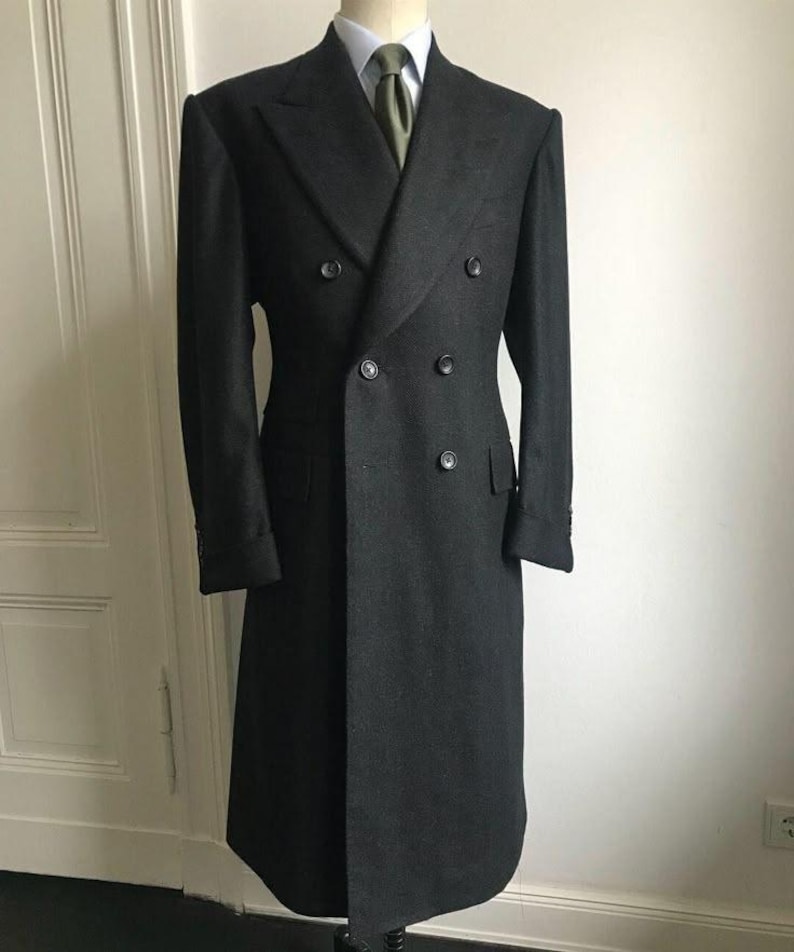 Puede incluir: Un abrigo cruzado gris antracita con seis botones, exhibido en un maniqu&iacute;. El abrigo presenta solapas con muescas, dos bolsillos delanteros y una silueta larga y entallada. Se ven una camisa blanca y una corbata verde oliva.