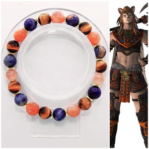 Puede incluir: Una pulsera de cuentas con una mezcla de piedras preciosas naranjas, azules y marrones. La pulsera se exhibe sobre un soporte circular transparente. Las piedras preciosas son redondas y miden aproximadamente 1 cm de diámetro. La pulsera está adornada con cuentas doradas.