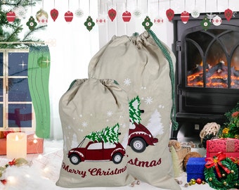 May include: Two beige Christmas gift bags with green drawstrings. Each bag features a red car carrying a green Christmas tree, white snowflakes, and the words "Merry Christmas" in red. The bags are on a white surface.