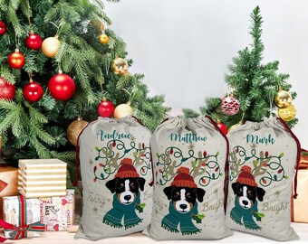 May include: Three beige Christmas gift bags with drawstring closures. Each bag features a dog wearing a hat and scarf, with the names "Andrew", "Matthew", and "Mark" above. The bags are decorated with Christmas lights and the words "Merry & Bright".
