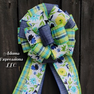 May include: A large, blue, green, and white bow with a floral pattern. The bow is made of ribbon and is tied in a knot. The bow is on a wooden background.