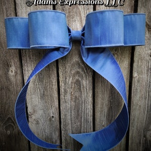 May include: A large, blue decorative bow with a textured finish. The bow is made of a wide ribbon and has multiple loops and long, flowing tails. The bow is mounted on a weathered wooden background. The text "Adams Expressions LLC" is in the upper left corner.
