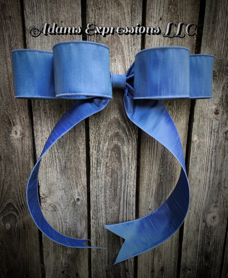 May include: A large, blue decorative bow with a textured finish. The bow features two large loops on each side and long, flowing tails. The background is a rustic wooden surface. The text "Adams Expressions LLC" is visible at the top.