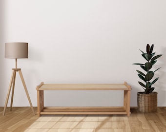 Op de afbeelding: Een houten plank met twee planken, een lichtbruine lamp met een beige lampenkap en een plant in een gevlochten mand met donkergroene bladeren.