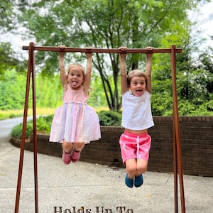 Ash wood clothing rack holding up to 60 lbs – strong enough for multiple items. Shown with two kids hanging, demonstrating stability and durability. Ideal for secure storage or display, combining function and style.